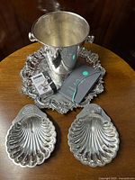 Top view of the silver plated footed salver with champagne cooler bucket, cork remover, two shell dishes, and champagne book arranged on a wooden table.