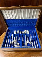 Photo of silver plated flatware displayed inside open walnut chest with blue velvet lining.