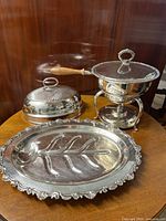Silver plated serving items: oval tray, meat dome, warming dish shown on wooden table.