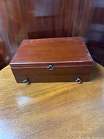 Closed mahogany finished silverware chest showing front side with metal handles and latch, standing on a wooden surface.