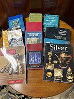 Photo showing 10 reference books on table about silver, glass, china collecting with visible titles on silver, pottery, porcelain marks, pressed glass.