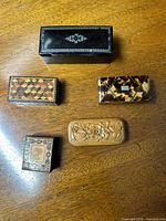 Top view of all five small antique boxes laid out on a wooden surface showing different materials and designs including tortoise shell, wood inlays, and carved details.