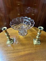 Photo showing the scalloped crystal tazza centered on wooden table flanked by two brass push-up candlesticks
