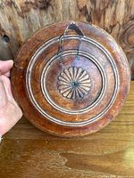 Front view of the wooden carved round lid or plate highlighting the carved floral center and concentric rings as well as the prominent crack.