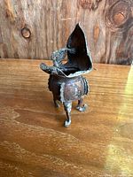 Front angled view showing the goblet's tripodal legs, ornate design, and damaged bent rim.