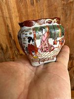 Mini porcelain vase held in hand showing hand-painted traditional Chinese women in robes, decorative reddish-brown rim with gold accents.