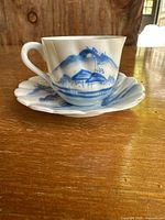 Side view of thin porcelain tea cup with blue Japanese landscape design on wooden table