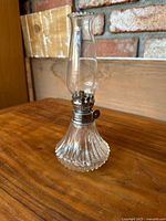 Full image of the antique oil lamp showing ribbed glass base and clear chimney with scalloped edge on wooden surface
