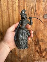 Full view of antique pewter figurine of a Victorian woman held in hand showing full body and dress details