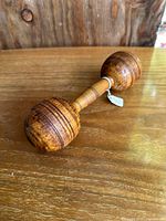 Side view of antique wooden dumbbell resting on wooden surface, showing full item length and shape.