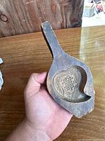 Photo of wooden mochi mold held in hand showing overall shape and handle, highlighting aged wood and carved cavity.