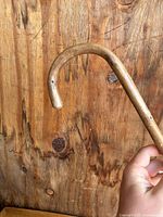 Close-up photo showing the curved handle of the wooden cane against a wood background.