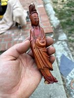 Close-up front view of the reddish-brown carved boxwood Guanyin figurine held in hand, showing detail and wood grain.