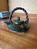 Mini green glazed teapot on a wooden surface.