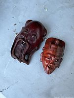 Two carved wooden masks of a Chinese man and woman displayed on a surface.