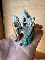 Three mudmen figurines shown resting on a palm, visible details of robes and facial features.