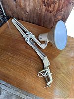 Full view of the clamp on workbench lamp with extended articulated arm and clamp base, lying on a wooden surface.