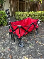Red collapsible wagon with black metal frame, fabric seating area and four wheels. Pull handle with rope attached.