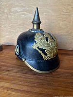 Front and side view of the black leather Pickelhaube helmet showing brass eagle emblem and spike.