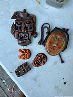 Overview of all six Asian masks arranged on a surface, showing varied sizes and designs, mostly wooden and carved.