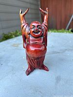 Wooden Hotei Buddha figurine standing on table, showing front view with arms raised.