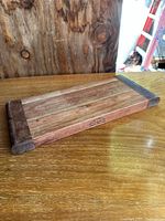 Rectangular wooden cutting board on a wooden surface, showing overall condition and darker end pieces.