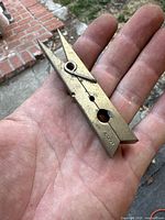 Clothing pick clip held in hand showing full clip and spring mechanism, Made of solid brass.