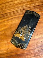 Black lacquered Japanese wooden panel featuring hand-painted gold lattice border and traditional Japanese garden scene with animals.