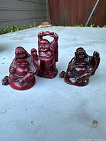 Three vintage Buddha figurines displayed outdoors, showing their different poses and red color with black detailing.