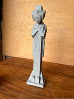 Photo of the full statue standing on wooden surface against a wooden background, clearly showing the entire front and base of the figure.