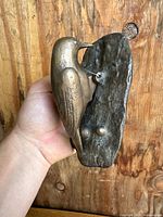 Front view of the bronze woodpecker door knocker held in hand against a wooden background showing detailed bird figure and textured backplate.
