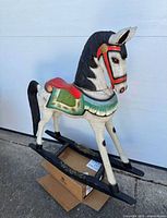 Side profile full view of the antique carved wooden rocking horse, sitting on a box for support, showcasing the whole body and base rockers with paint details.