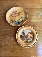 Two carved wooden plates shown on a wood surface, one with painted Nurnberg town scene, the other with carved German text and floral decoration