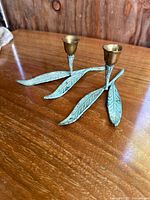 Pair of bronze leaf candle holders on a wooden surface, showing the leaf-shaped base and bronze candle cup.