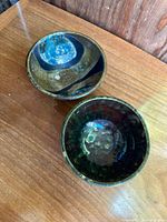 Two handmade Japanese styled ceramic bowls shown from top, colors range from blue to green and black with artistic glaze