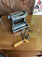 Stainless steel pasta roller and cutter set with hand crank and clamp on wooden table