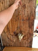 Photo showing the entire hanging smoke sprayer or candle holder suspended with hand holding the top ring against wooden background to display size and structure.