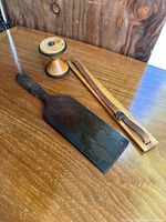 Three wooden antique items: paddle-shaped tool, wooden spool, and wooden strap holder on wood surface