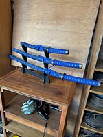 Full view of the three katana swords resting on the wooden stand, showing the blue handles and speckled sheaths.