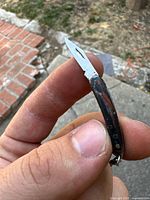 Miniature pocket cutter held between fingers showing blade and handle detail