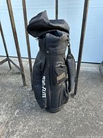 Full side view of the black Top Elite golf bag standing upright on a concrete surface, showing the bag shape and the brand name printed.