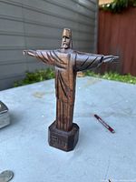 Full view of the carved wooden statue showing outstretched arms and octagonal base with engraving.