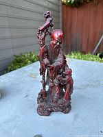 Front-side view of the carved vintage Chinese elder statue with a child, standing on a textured base outdoors.