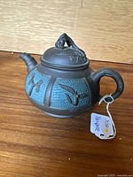 Front angle view of the teapot showing textured turquoise panels and carved floral motifs.