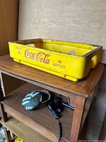 Yellow Coca-Cola plastic carrier case side view showing logo on one side and some dirt and wear on surface