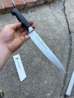 Knife held in hand showing full length with black handle and blade.