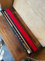 Full view of the pool cue disassembled inside the open carrying case showing the two-piece cue and red velvet interior.