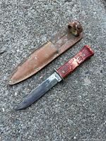 Knife with moose handle laid on ground next to worn leather scabbard