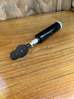 Side view image of the ophthalmoloscope showing long black handle and multi-lens round head.