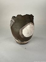 Front left side view showing the dark clay body with contrasting white cracked glaze patch and chipped irregular rim.